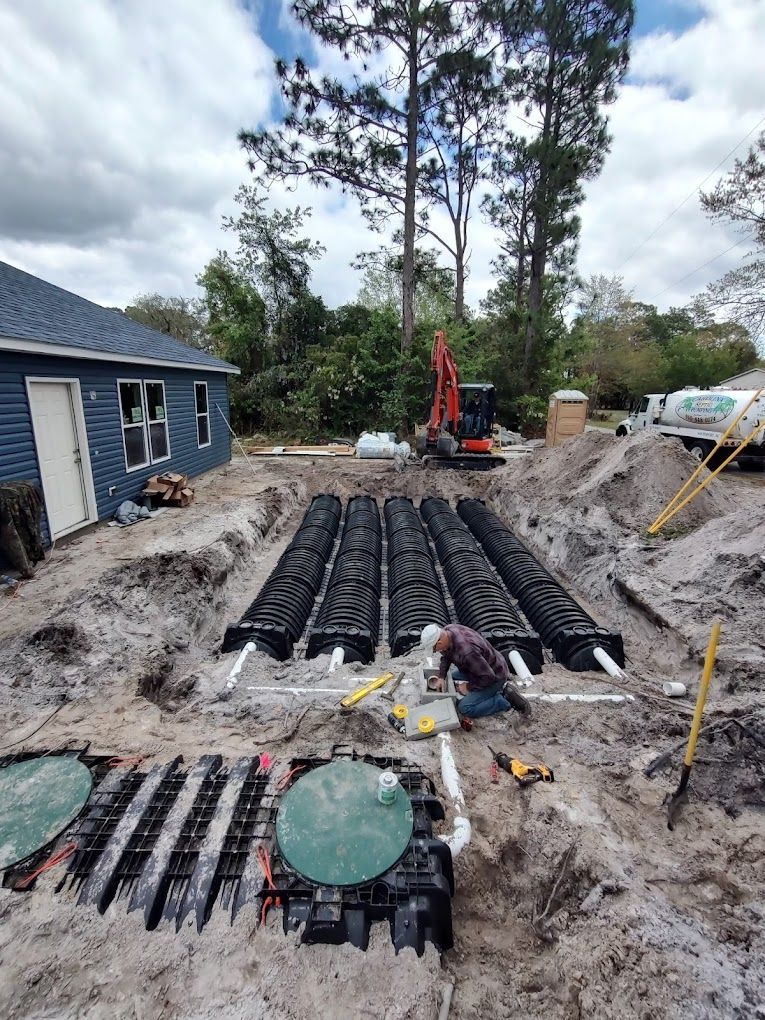 A man is working on a septic system in the dirt in front of a house.
