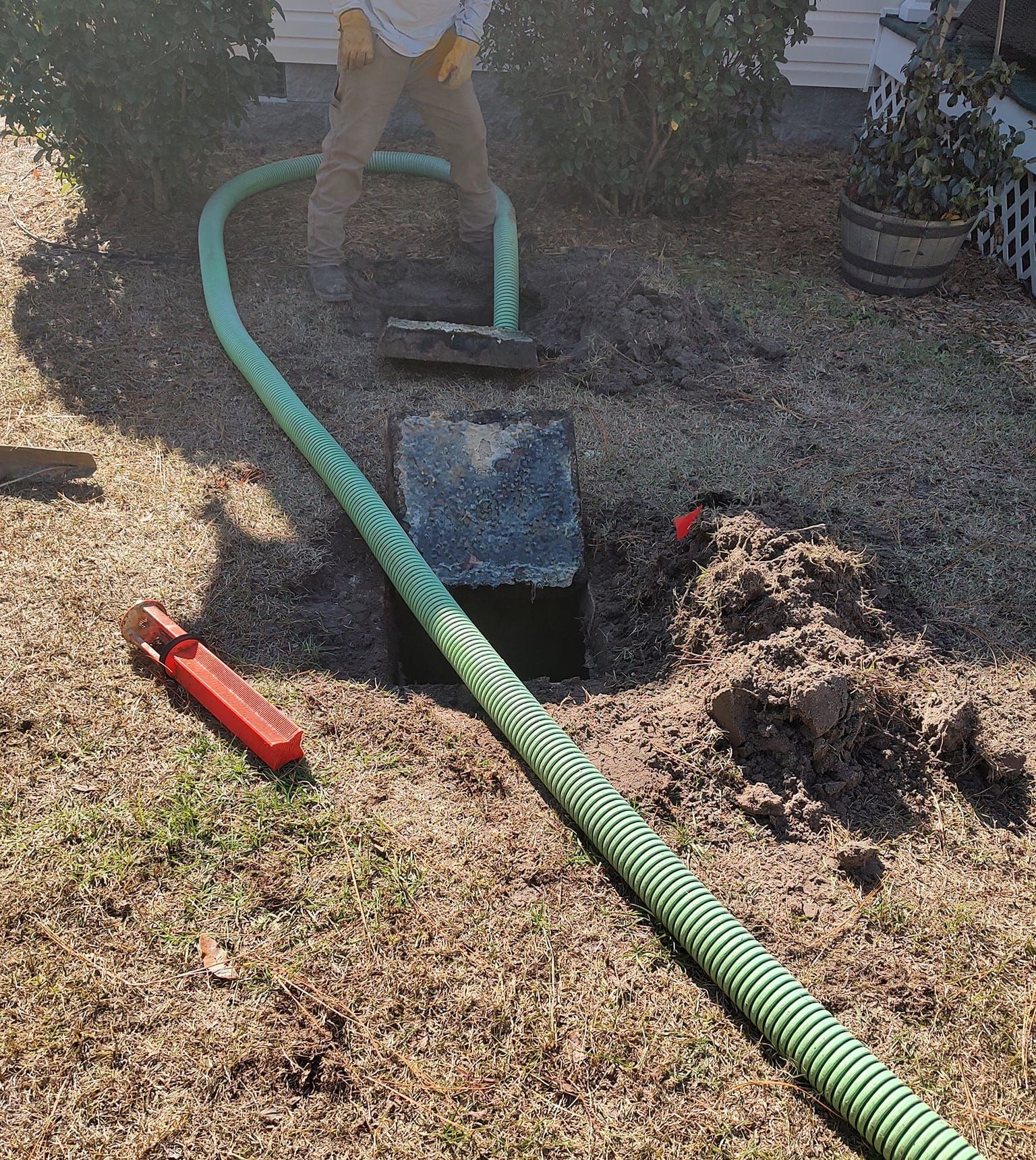 A man is standing next to a green hose in the dirt.