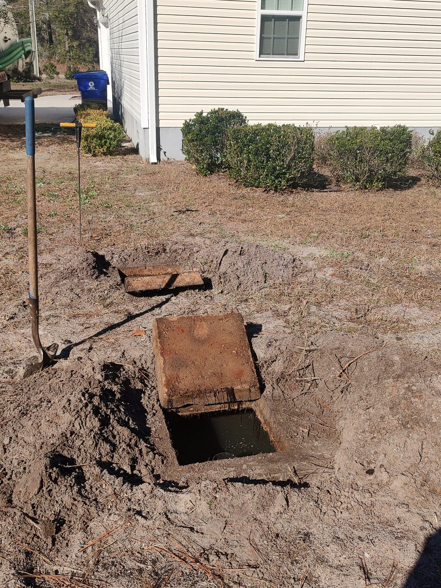 A manhole cover is sitting in the dirt in front of a house.