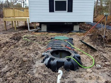 A septic tank is sitting in the dirt in front of a house.
