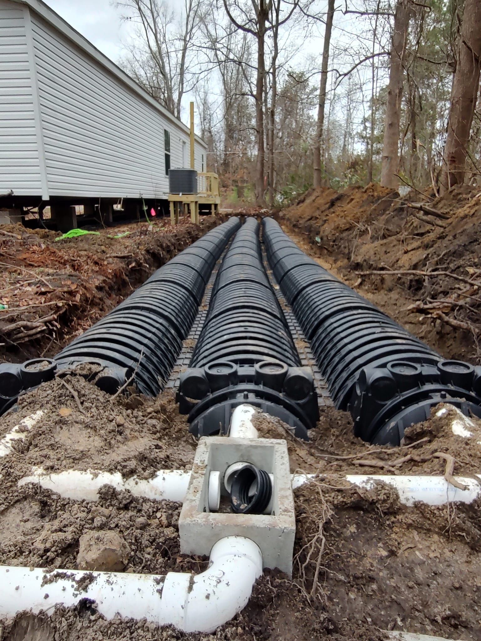 A drainage system is being installed in the dirt in front of a house.