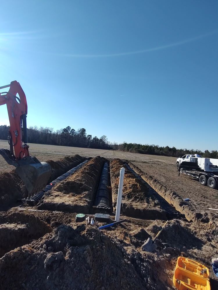 An excavator is digging a trench in a dirt field.