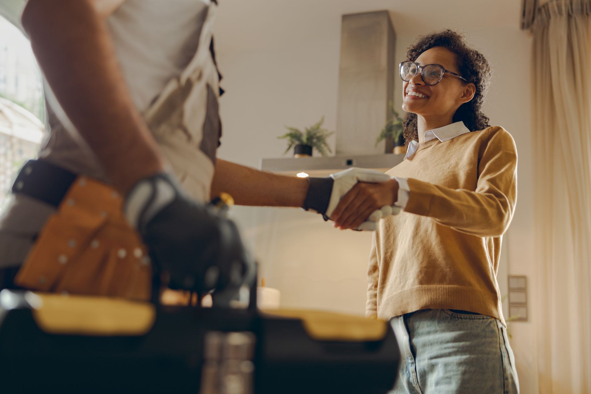 Woman shaking hands with repair person in kitchen, smiling.