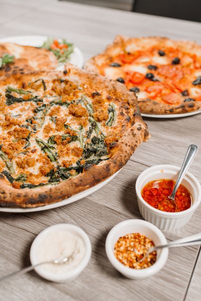 Two herb-topped pizzas on plates with dipping sauces on a table.