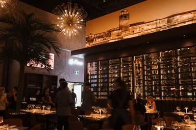 Dimly lit restaurant with diners, warm candlelight, wall shelves, and festive decorations overhead