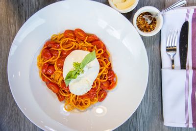 Plate of spaghetti with tomato sauce and mozzarella on a white dinner table setting, with cutlery and condiments