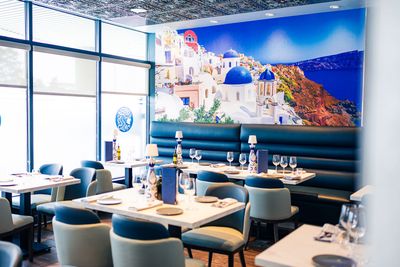 Bright seaside restaurant with blue-and-white decor, set tables, and a large coastal mural on the wall