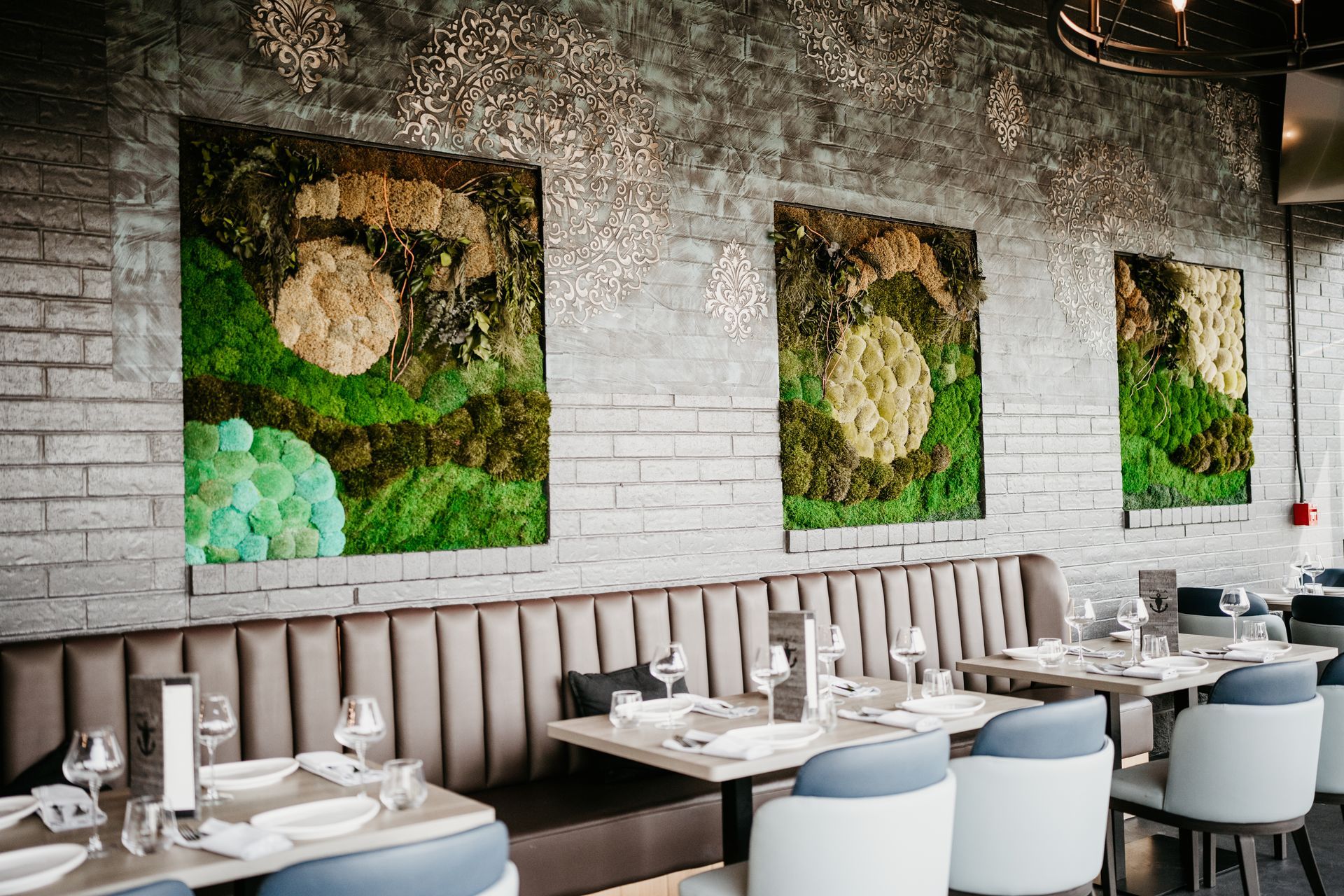 Modern restaurant dining room with white tables, gray chairs, and green wall art on a brick wall
