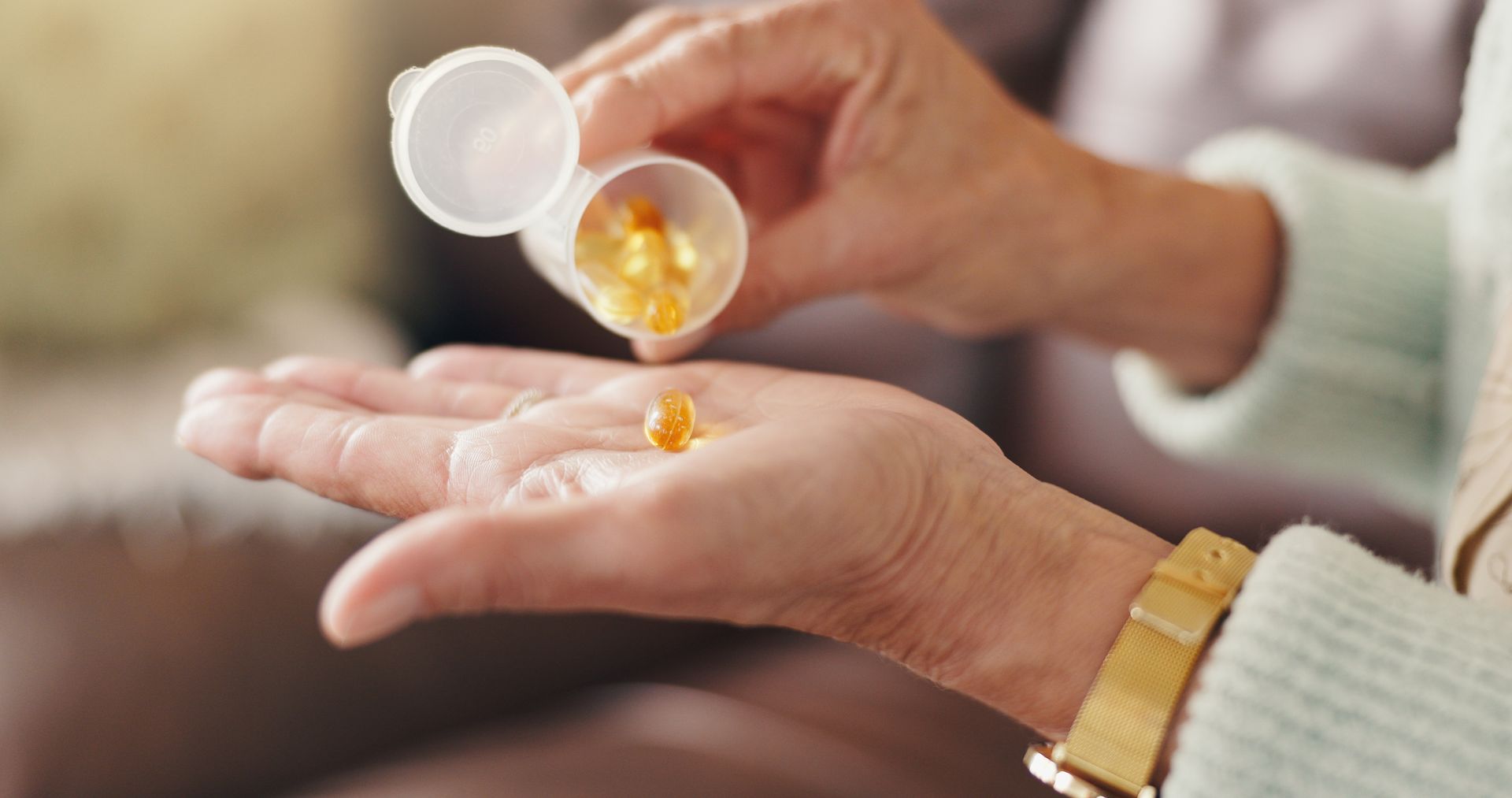An older adult pours softgel capsules from a small container into an open hand.