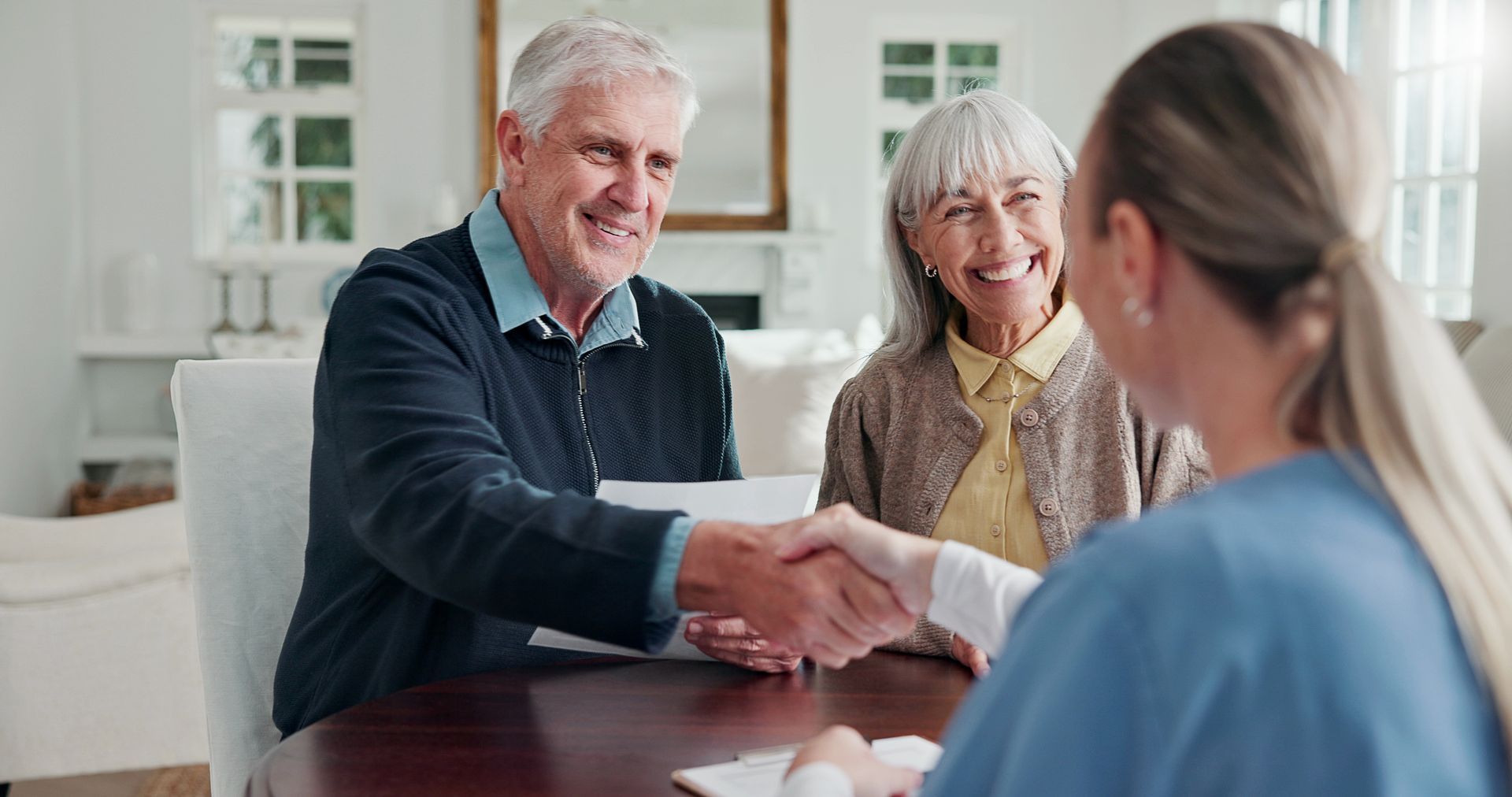 Senior couple shaking hands with a nurse during a home care consultation.