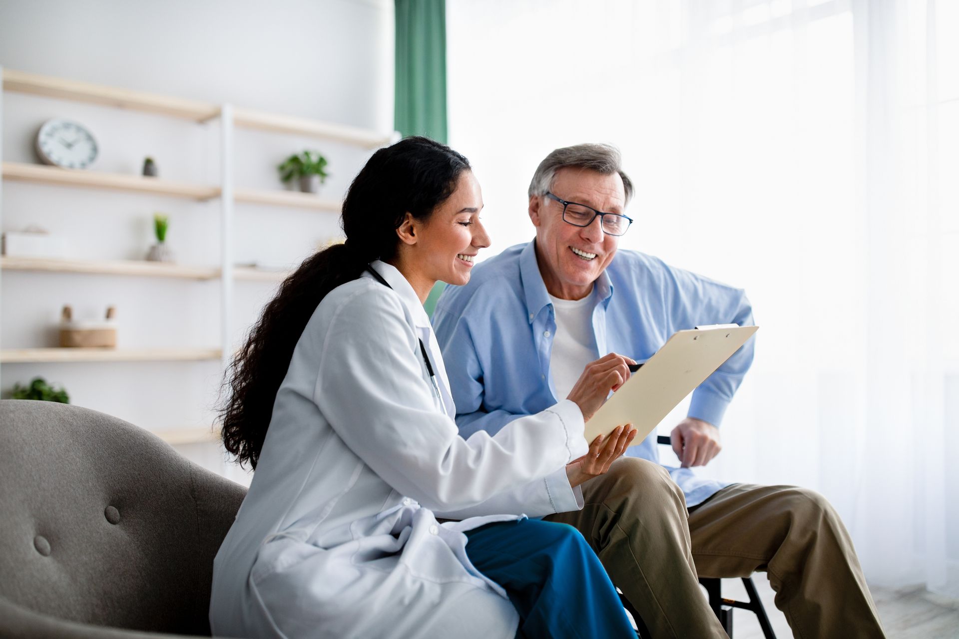 Young doctor asking senior impaired male patient in wheelchair to sign insurance policy at home. Young doctor asking senior impaired male patient in wheelchair to sign insurance policy at home.