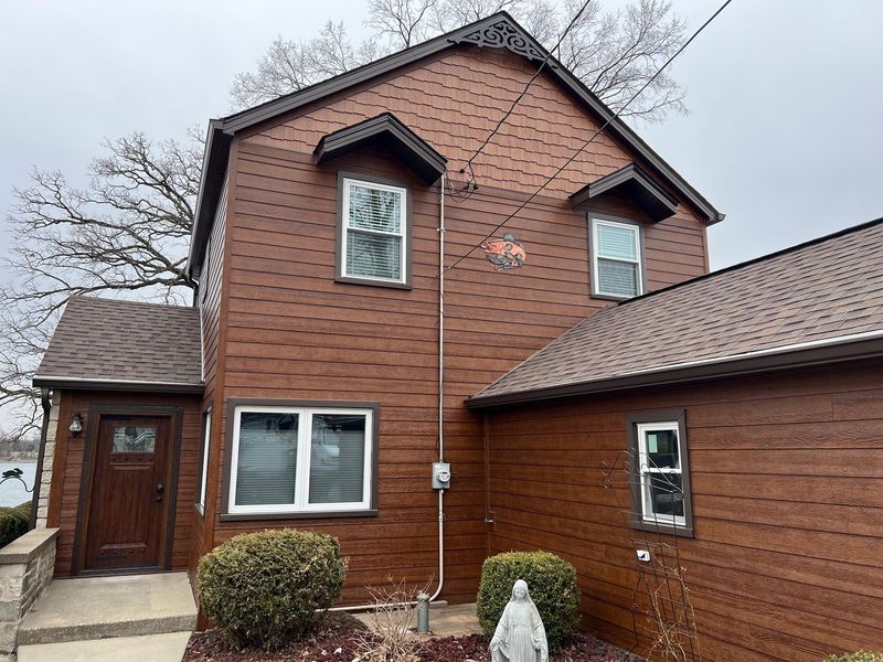 Exterior side view of a house with beige horizontal siding, white trim, multiple windows, and two potted plants outside.
