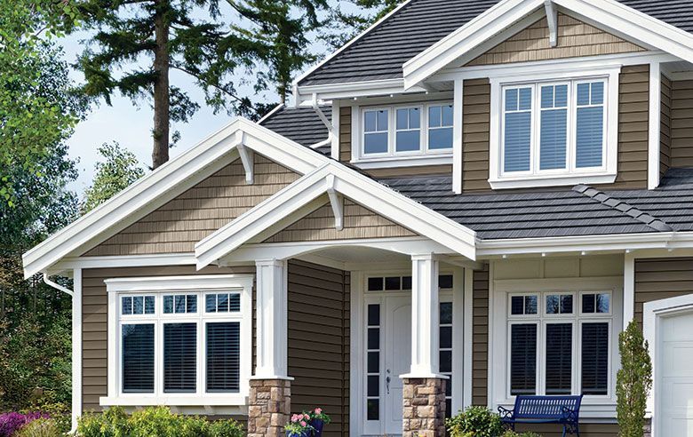 A multi-story house with dark siding, a gabled porch entrance with stone pillars, and white-trimmed windows.