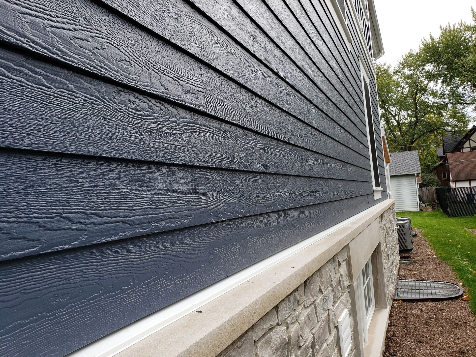 A close-up view of blue wood-grain siding installed above a stone foundation and beige concrete ledge on an exterior wall.