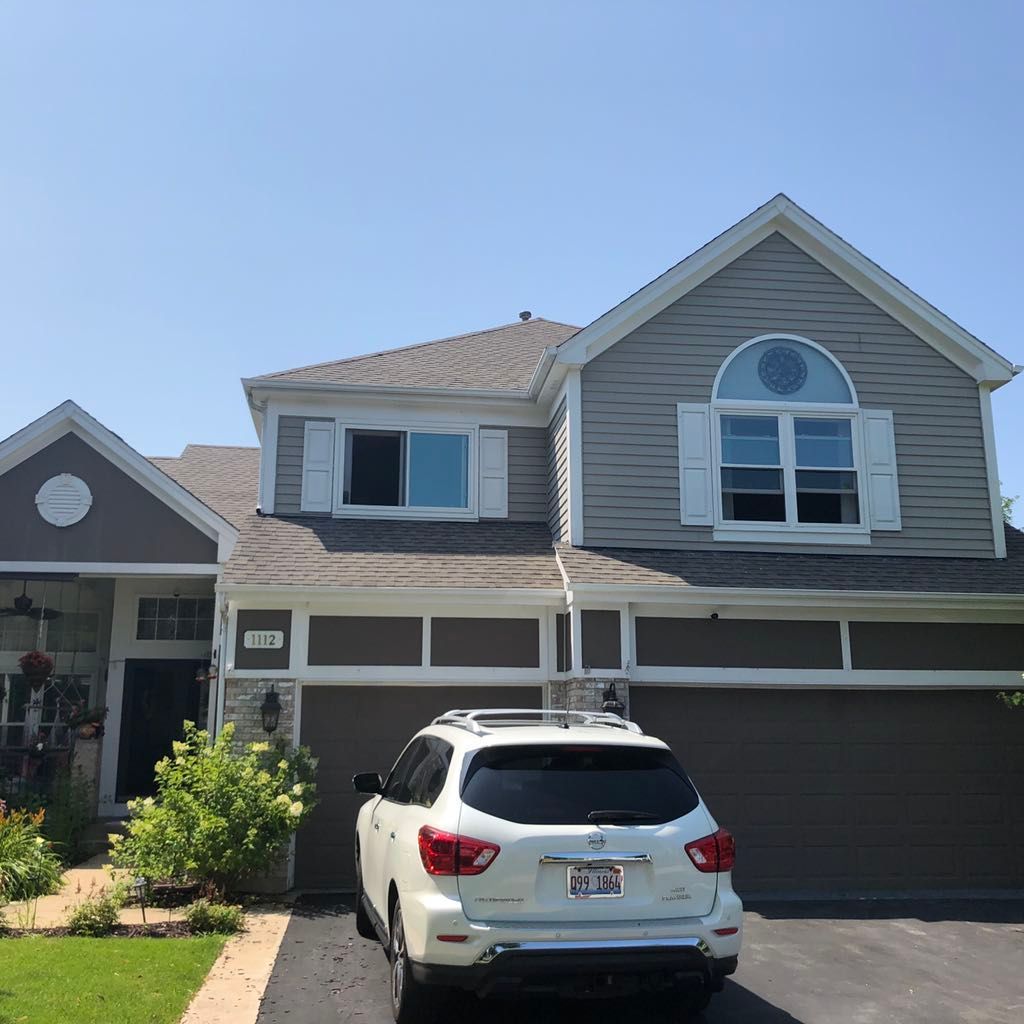 A two-story gray house with a white garage, arched window, and a white SUV parked in the driveway on a sunny day.