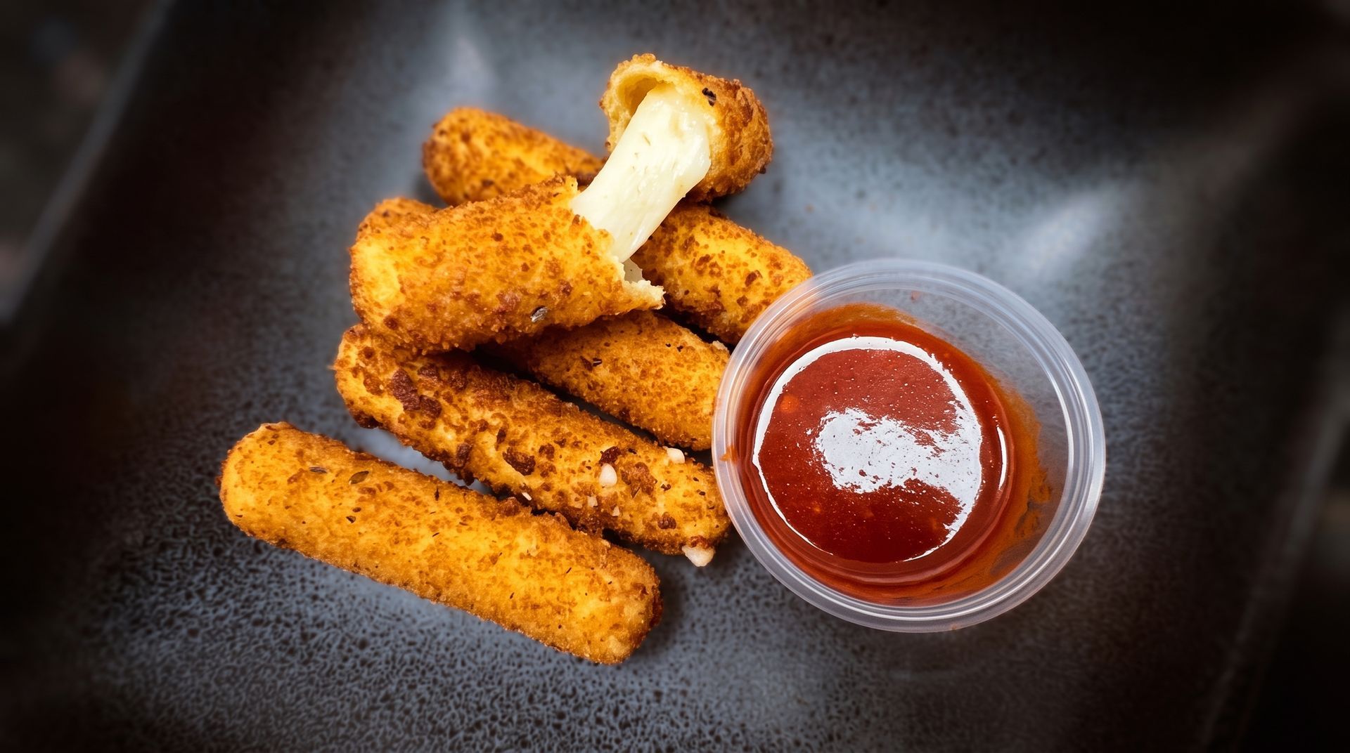 Breaded chicken tenders with dipping sauce in a black bowl