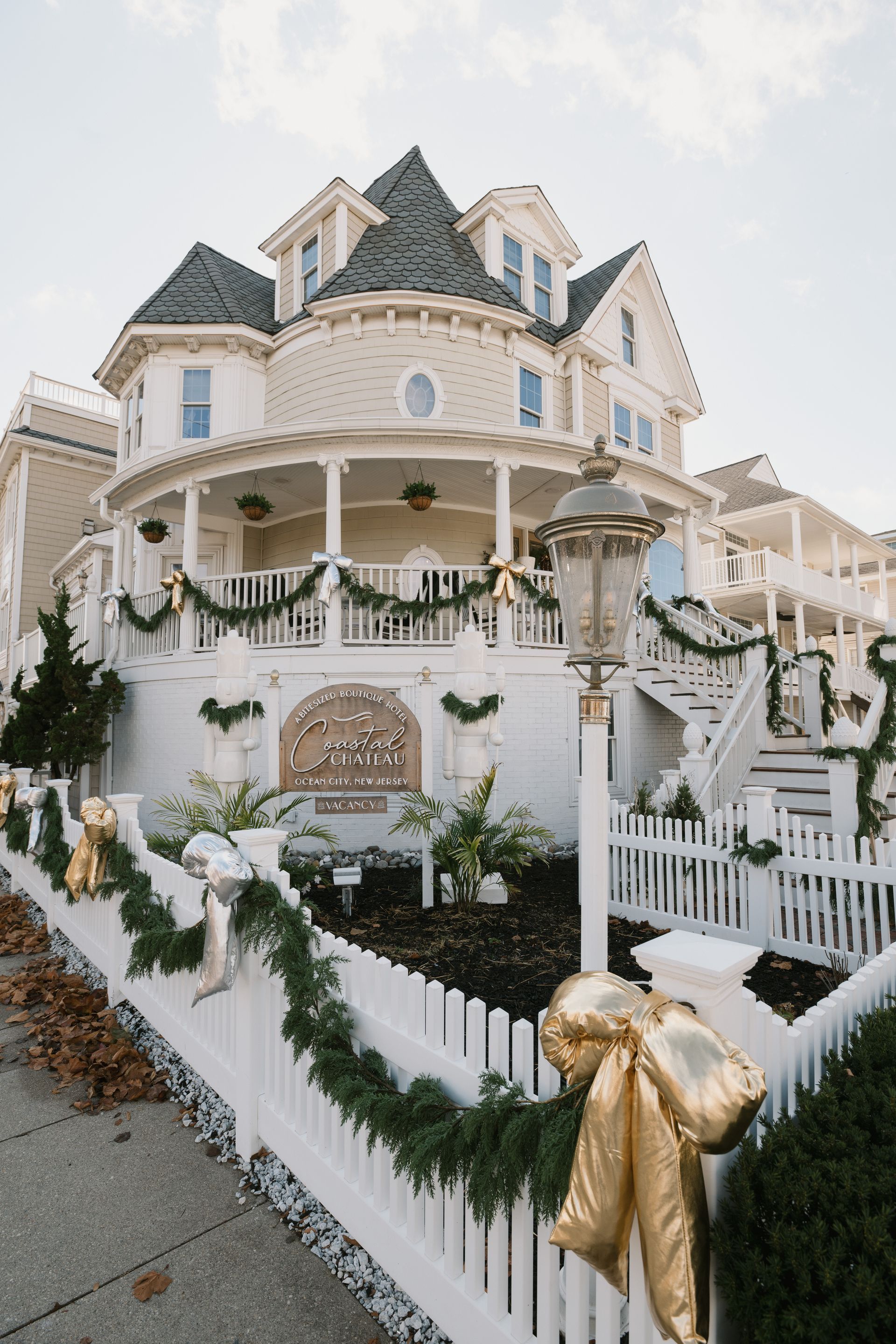 Festive Victorian house with white picket fence, adorned with garlands and gold bows.