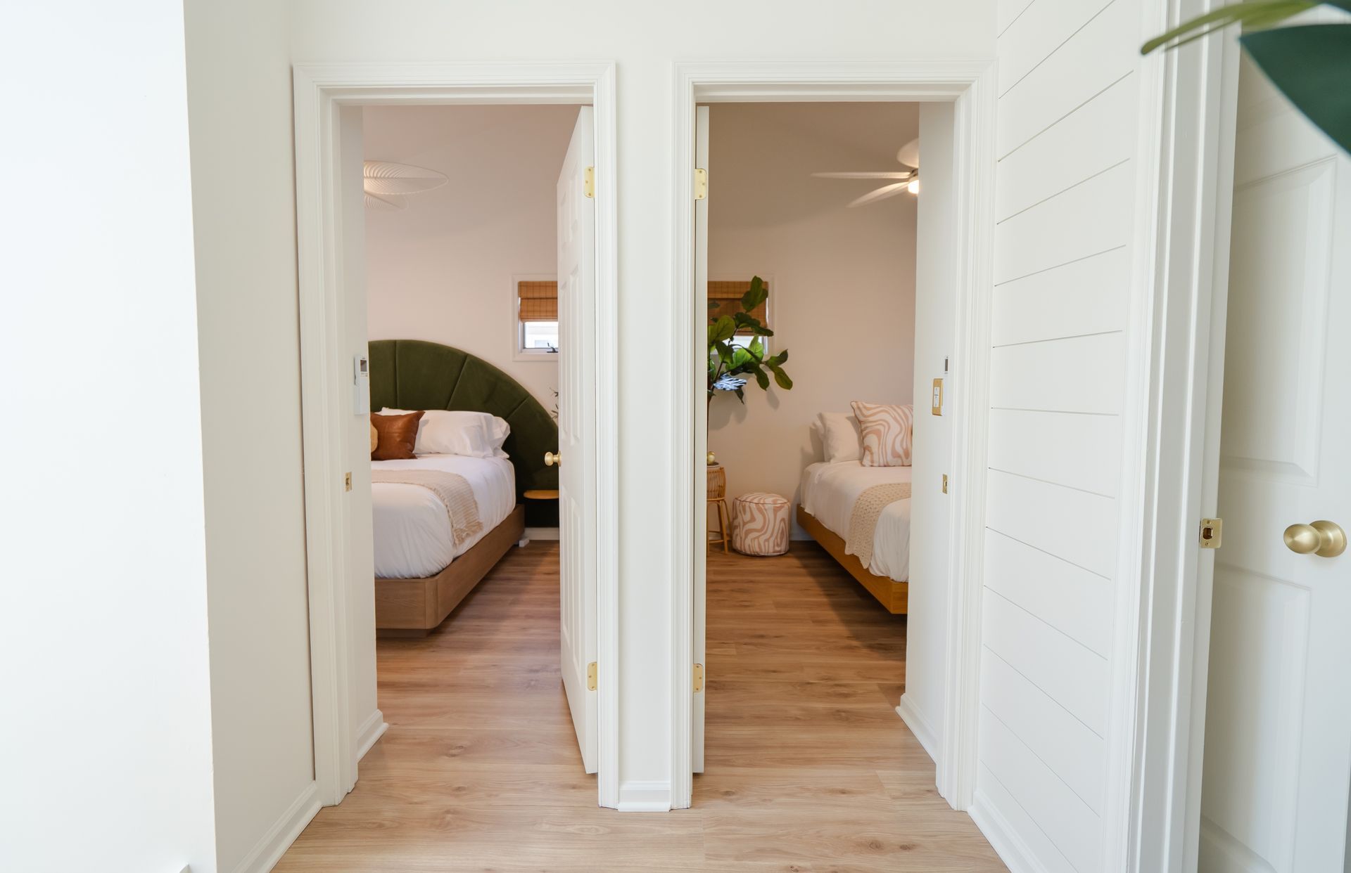 Hallway with open doors to two bright bedrooms, white walls, and light wood floors