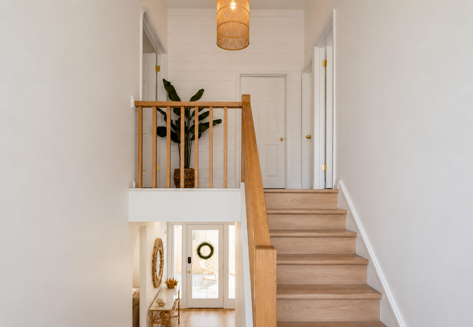 Bright hallway with carpeted stairs, wooden railing, pendant light, and a plant at the landing.