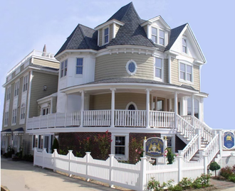 Victorian-style house with rounded porch, white picket fence, tan siding, and dark roof.