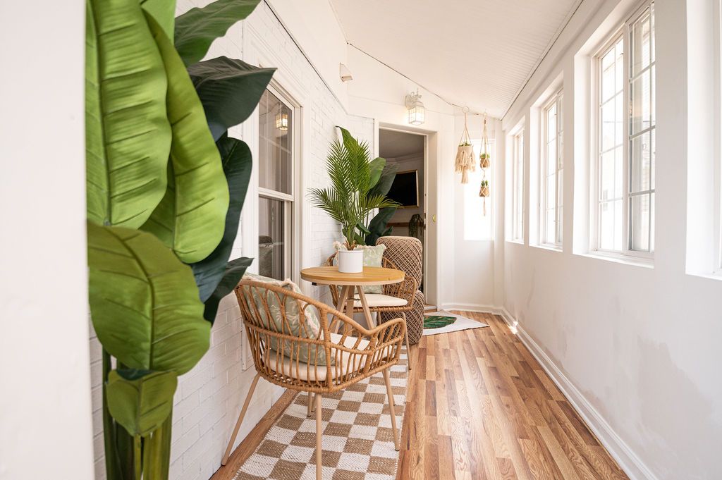 Sunroom with a rattan chair and table, potted plants, wood floor, white walls, and string lights.