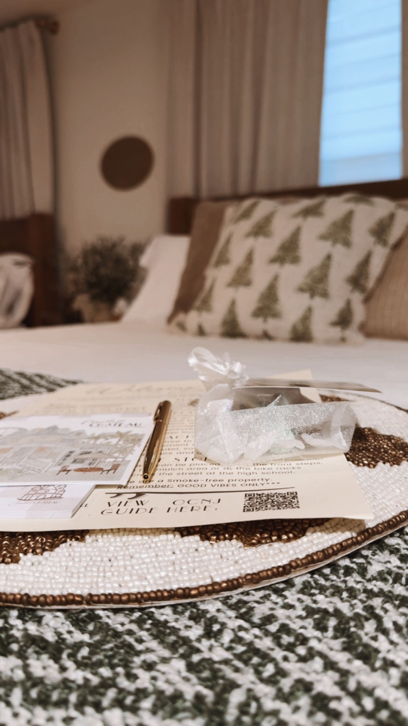 Bed with Christmas tree pillow, beaded tray with cards, and small wrapped gift.