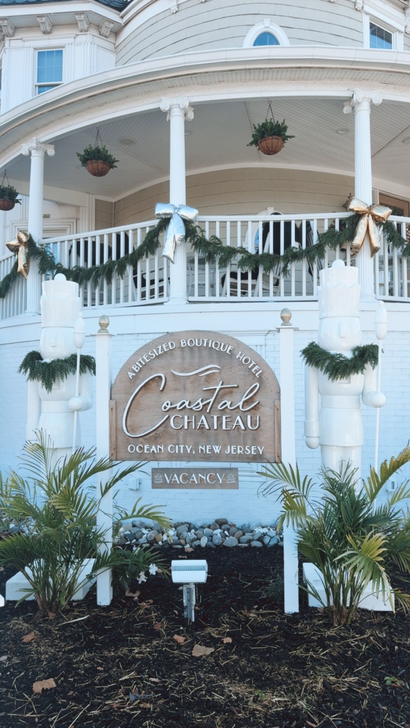 Sign for Coastal Heritage, with building in the background decorated for Christmas;  evergreens and bows.