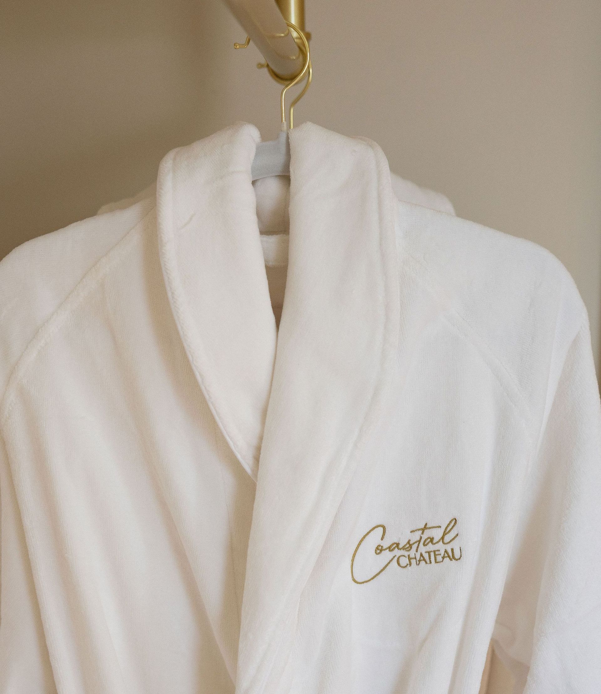White bathrobe hanging on a gold rod, embroidered
