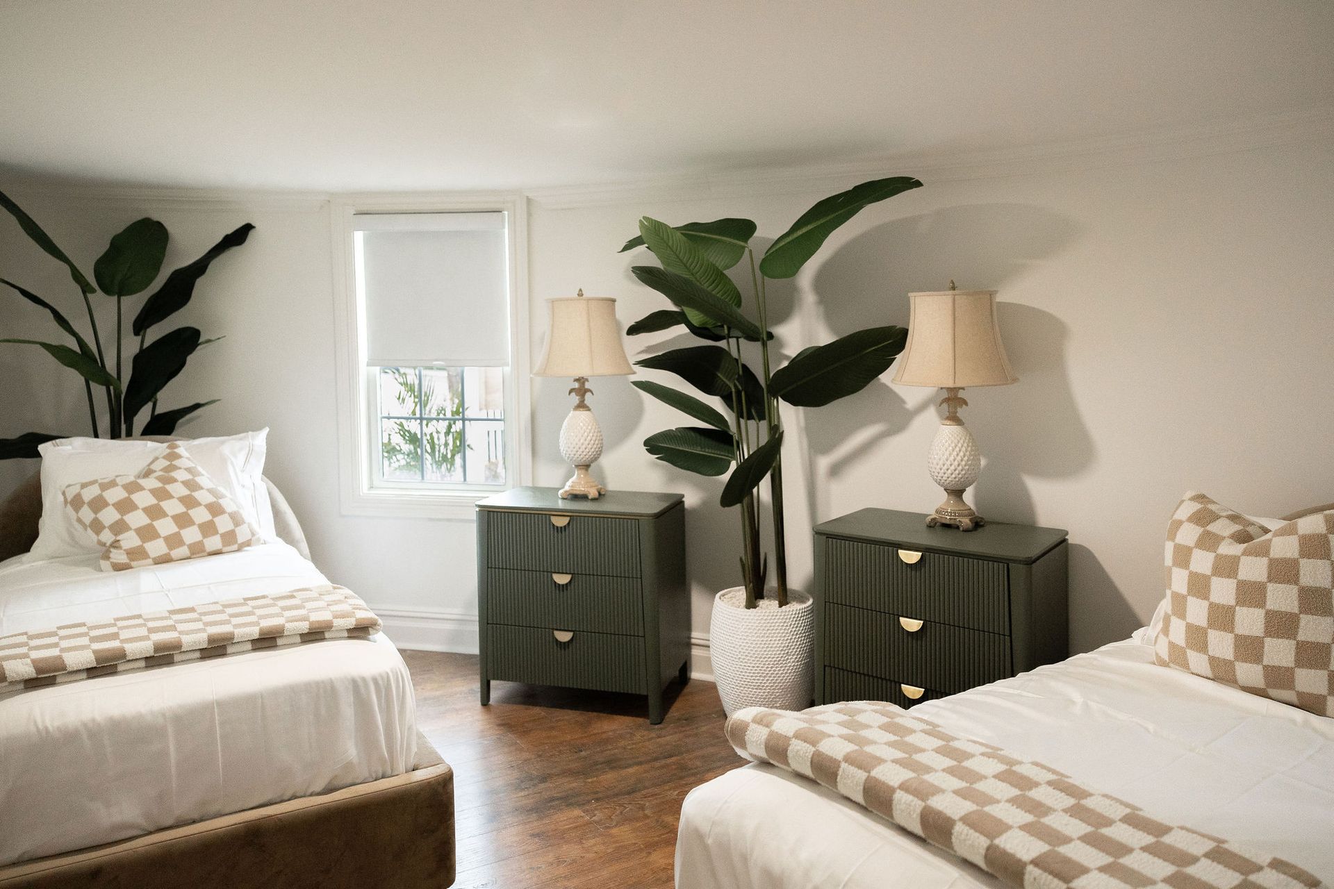 Two beds in a bedroom with green nightstands, lamps, and potted plants.