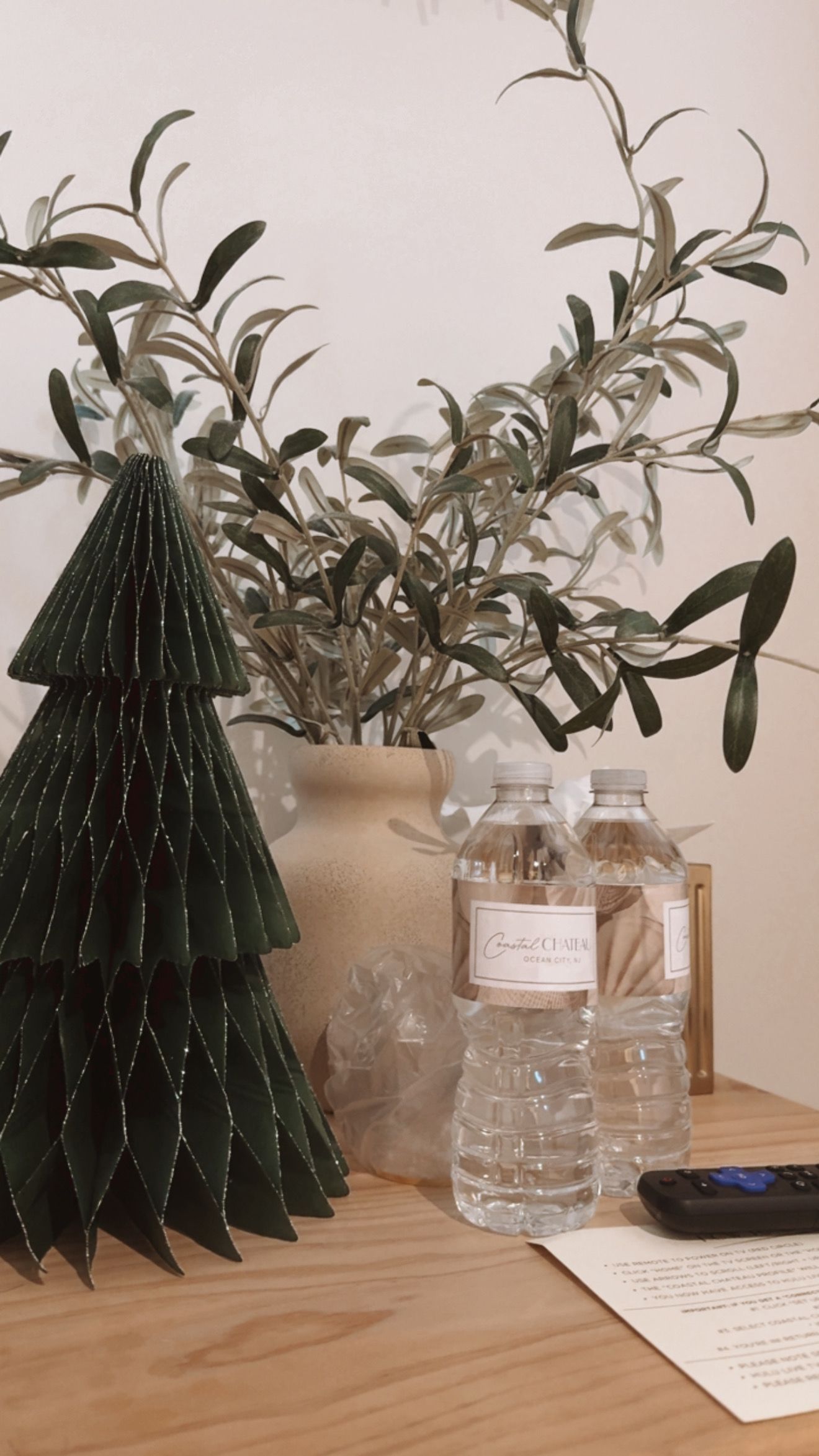 A decorative Christmas tree with a vase of branches, bottles, and a document on a wooden table.
