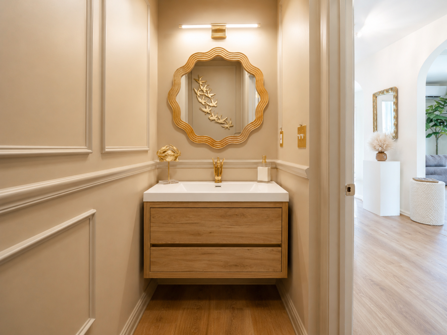 Elegant beige bathroom vanity with gold mirror, light wood cabinet, and wall sconces
