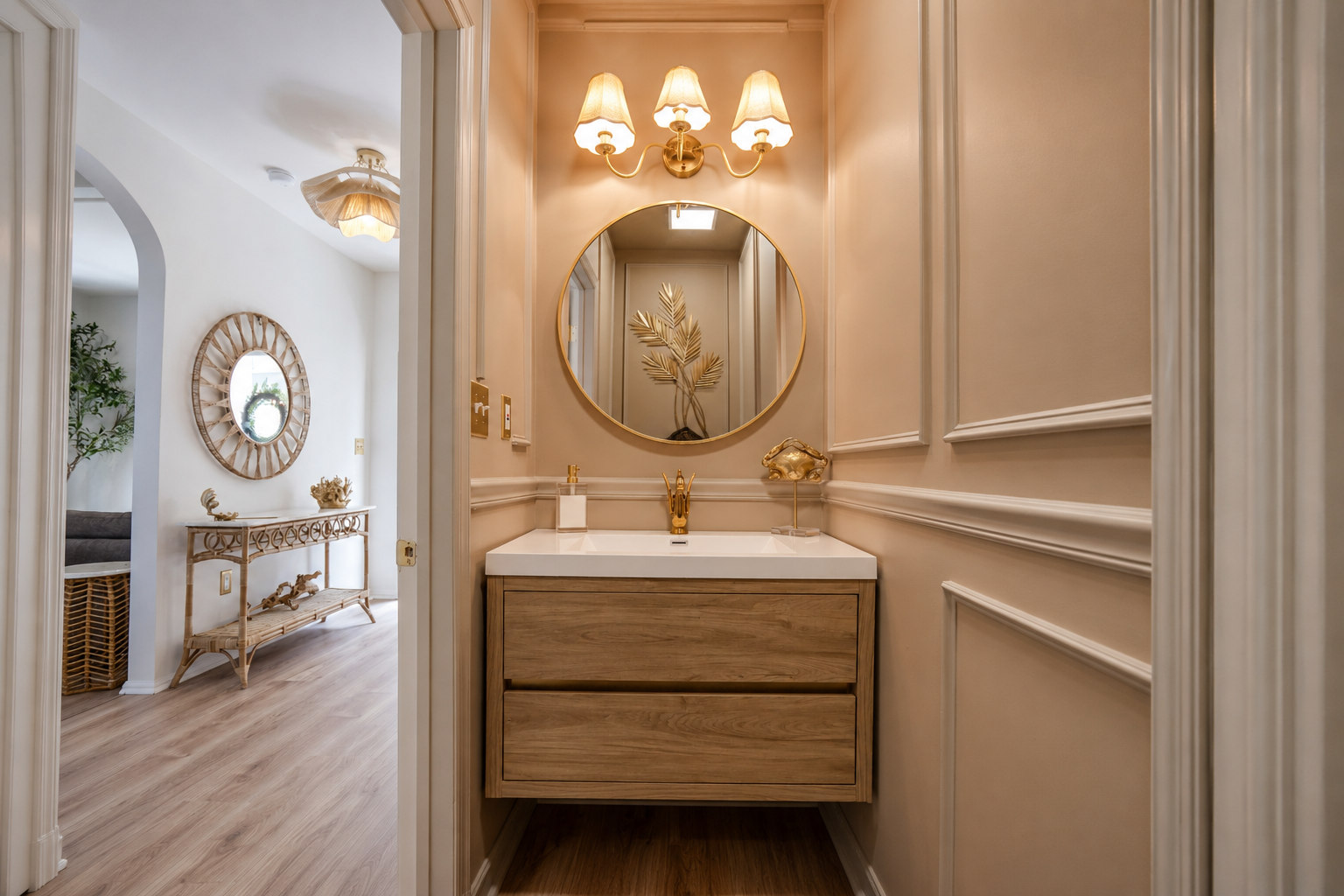 Elegant beige hallway with a round mirror, vanity sink, and chandelier lighting, leading to a bright room