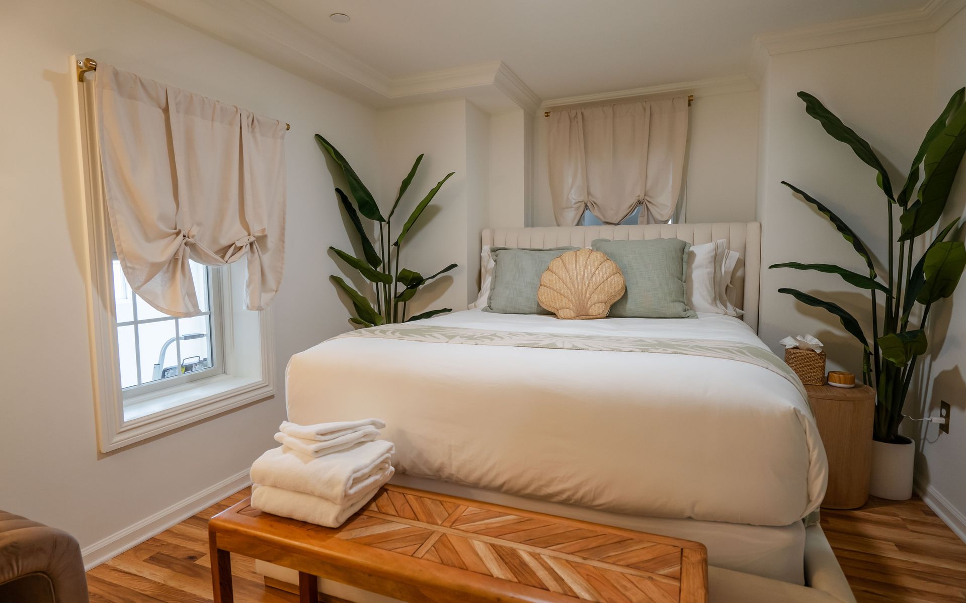 Bedroom with a bed, plants, window, and wood bench, decorated with a beach theme.
