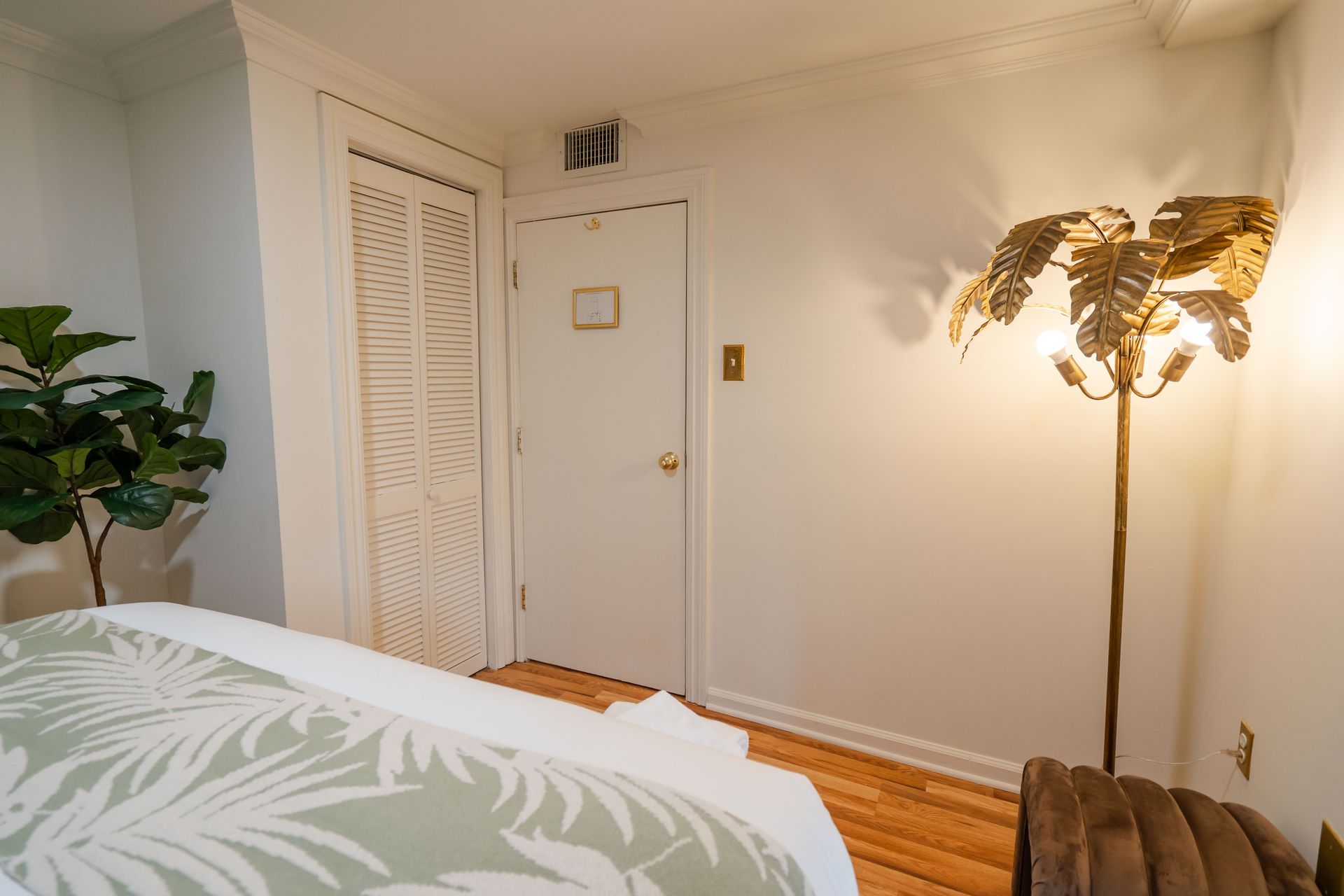 Bedroom interior with white walls, closet, closed door, bed with green pattern, and floor lamp.