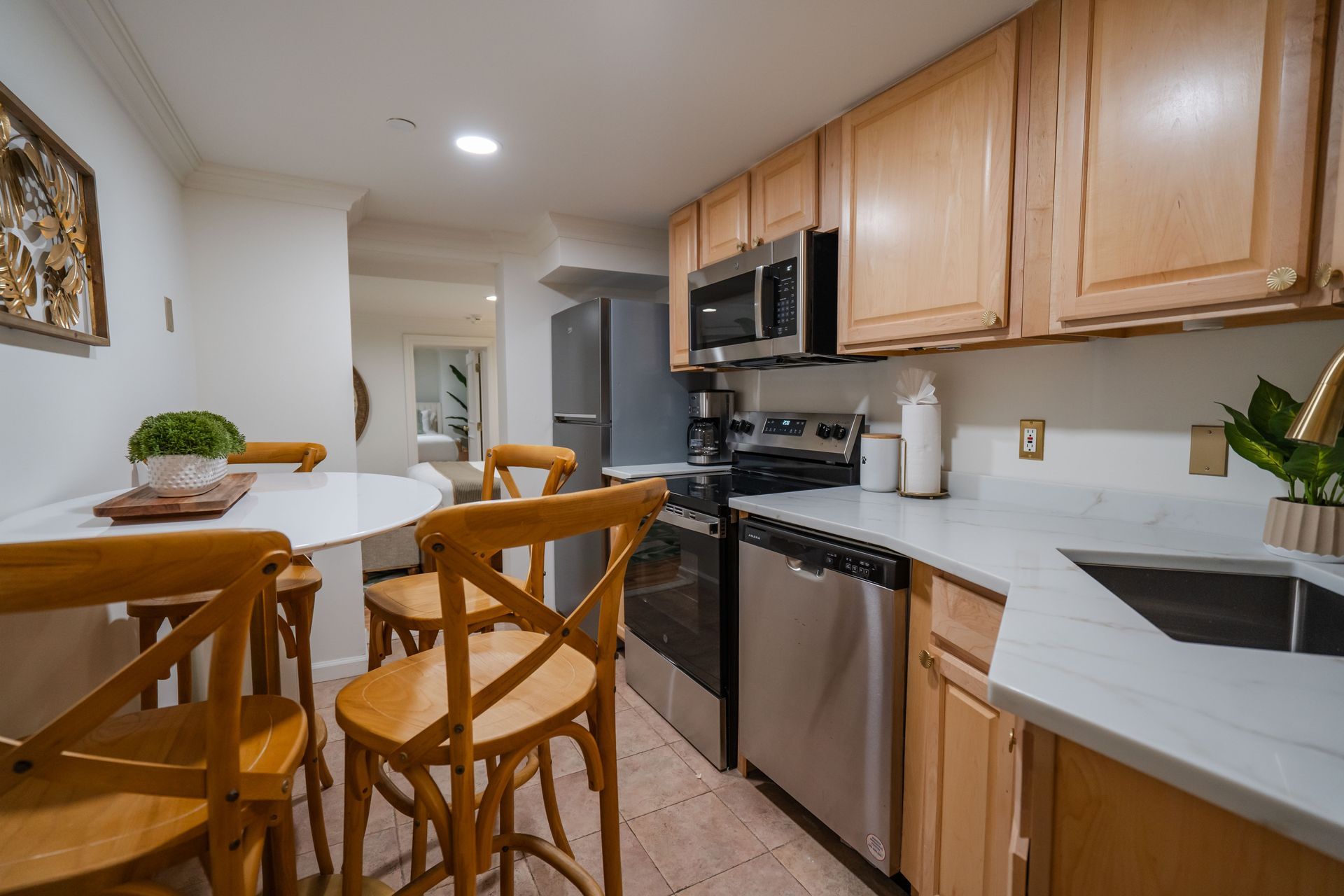 Kitchen with light wood cabinets, stainless steel appliances, and a small dining table with wooden chairs.