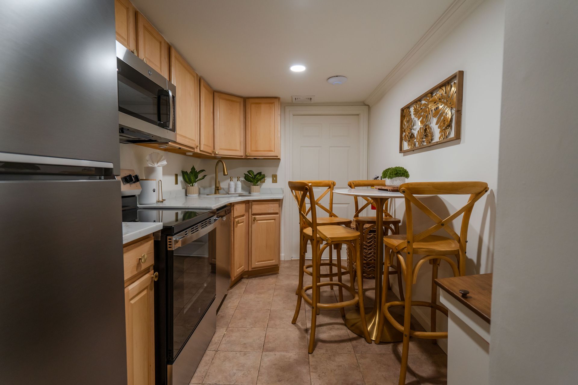 Small kitchen with light wood cabinets, stainless steel appliances, and a small table with three stools.