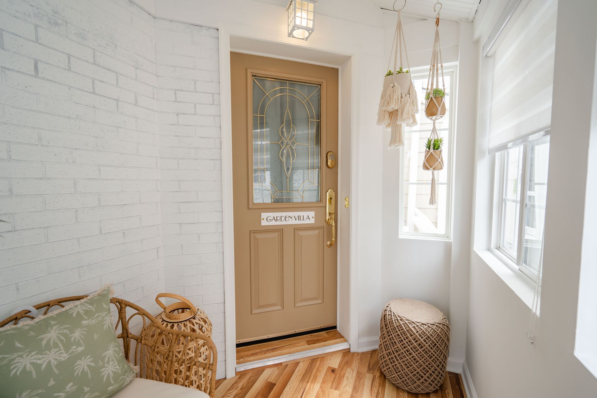 Beige entryway with wood floor, white brick wall, wooden door, and hanging plants.