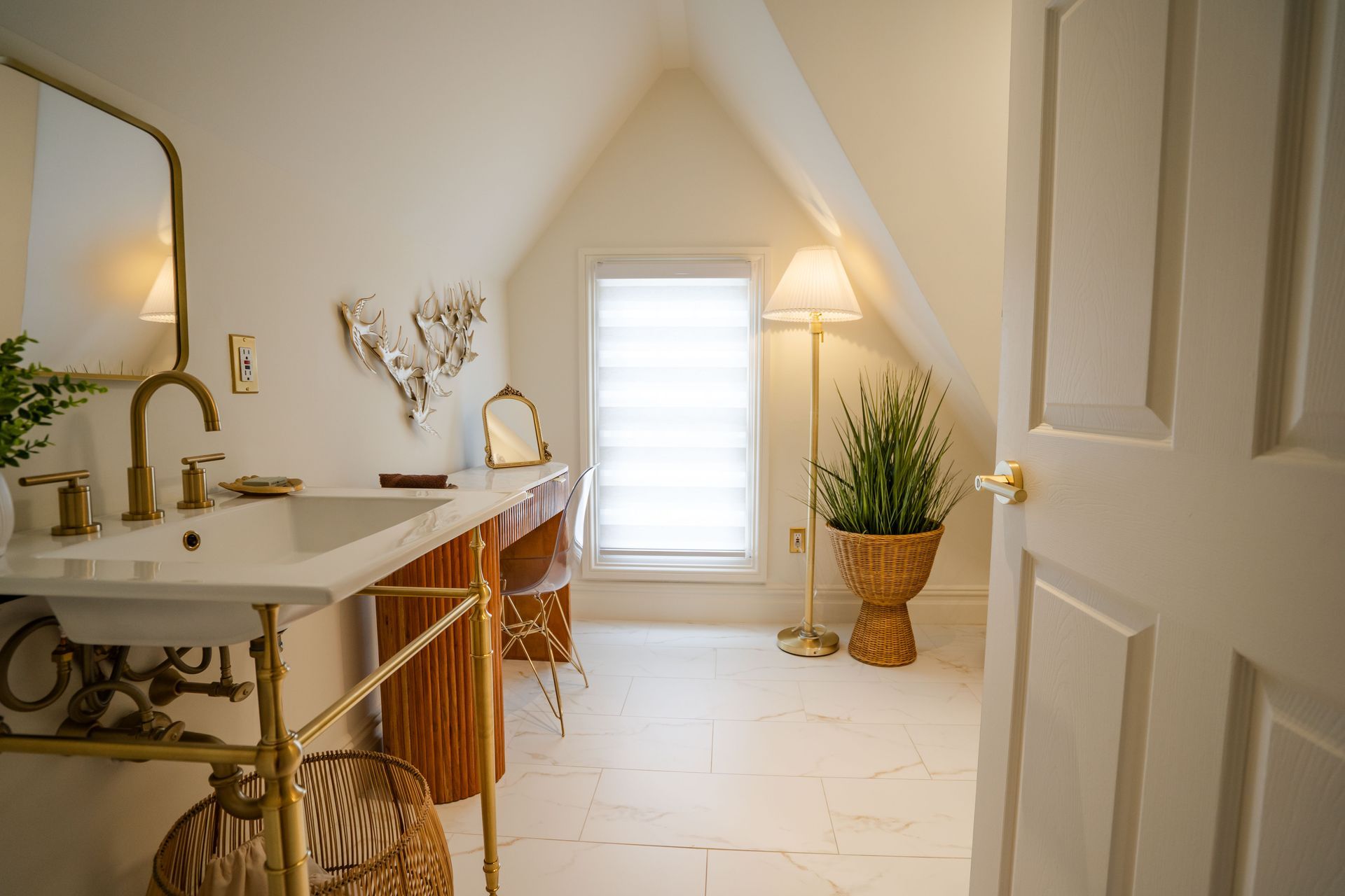 Bathroom with angled ceiling, vanity, gold fixtures, window, floor lamp, and white door.