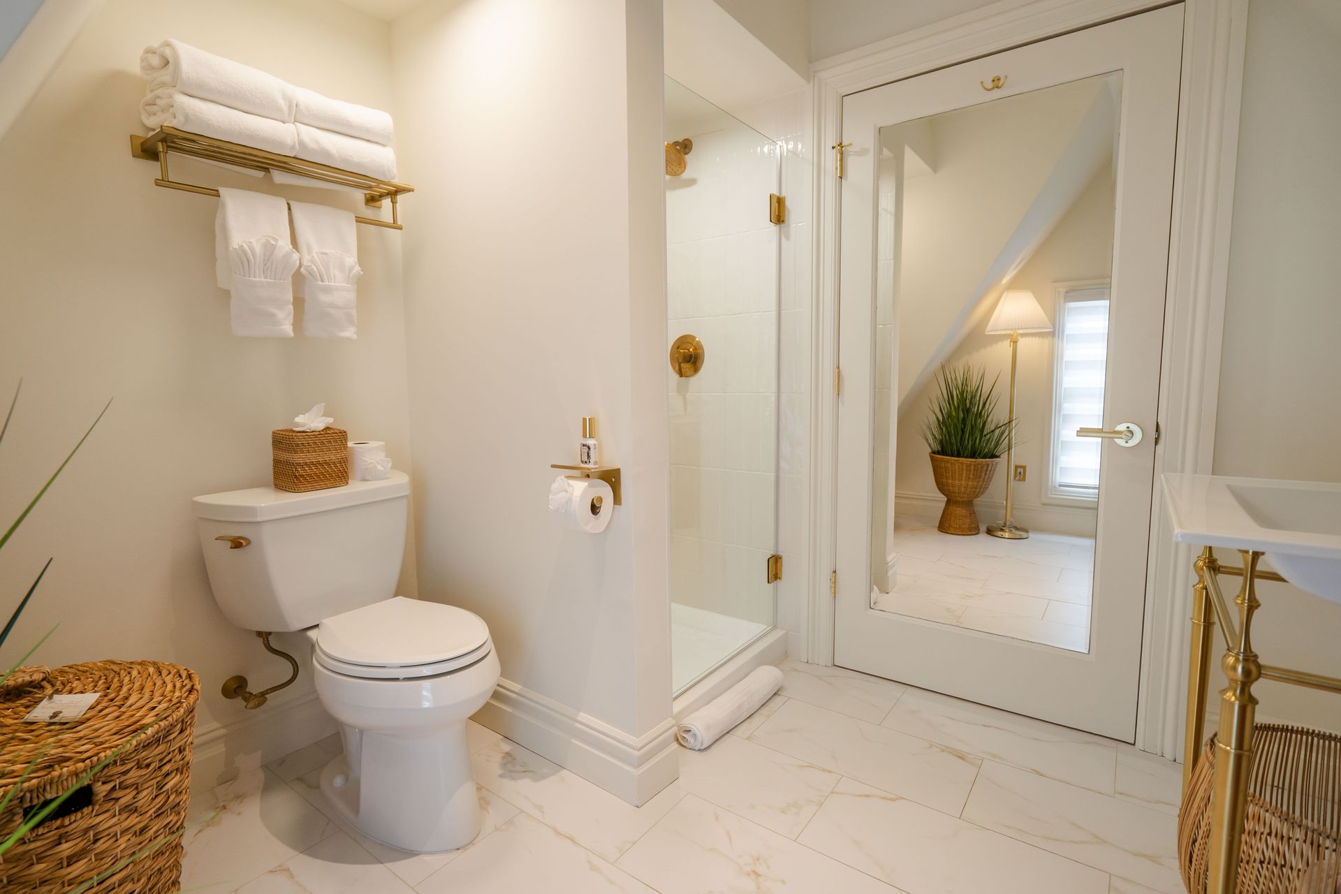 Bright white bathroom with a toilet, shower, and towels on a rack.