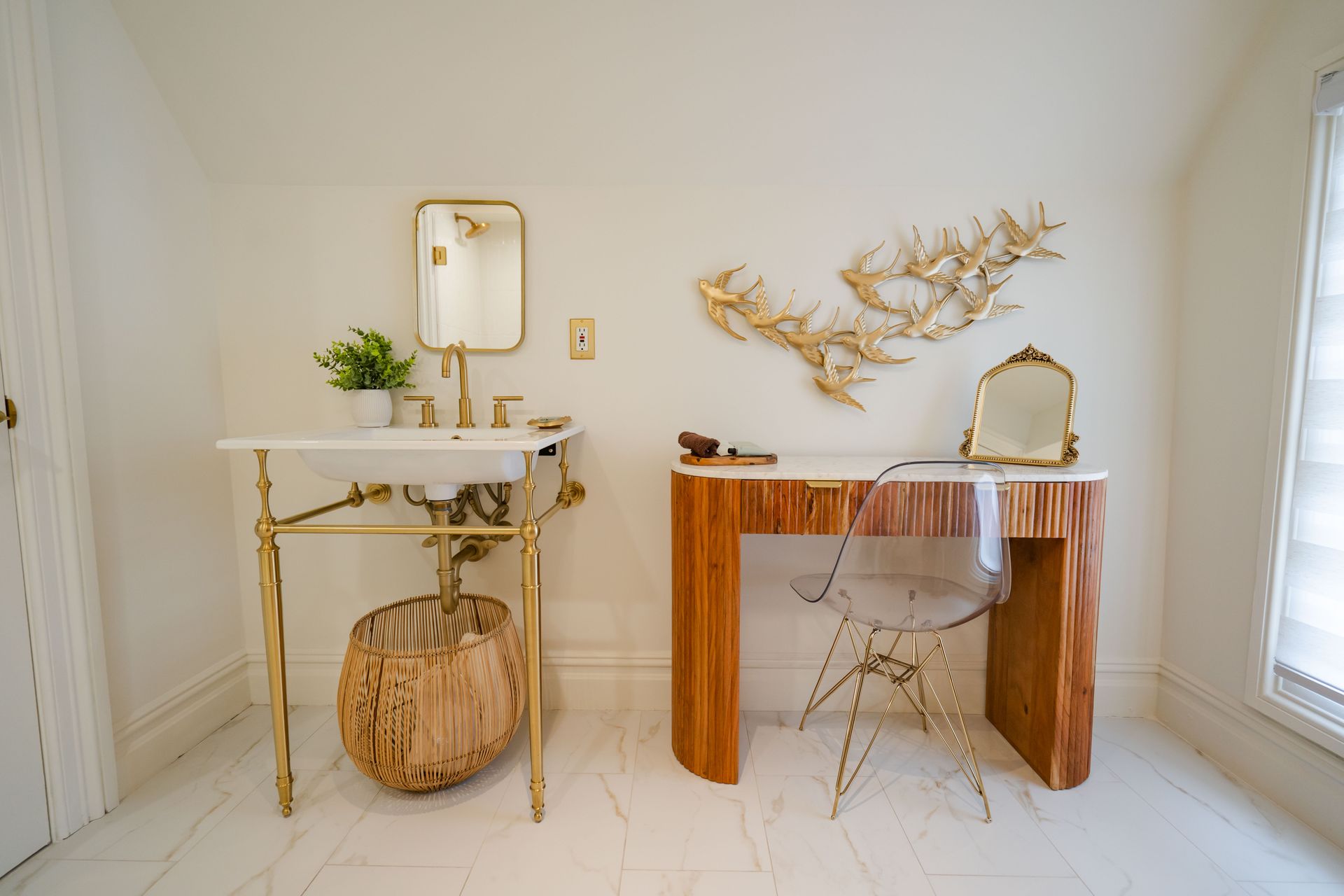 Bathroom with gold fixtures, marble countertop sink, wood desk, clear chair, and gold wall decor.
