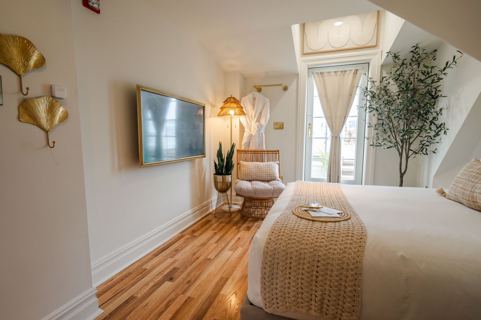 Bedroom with hardwood floors, bed, TV, chair, and large windows with curtains.