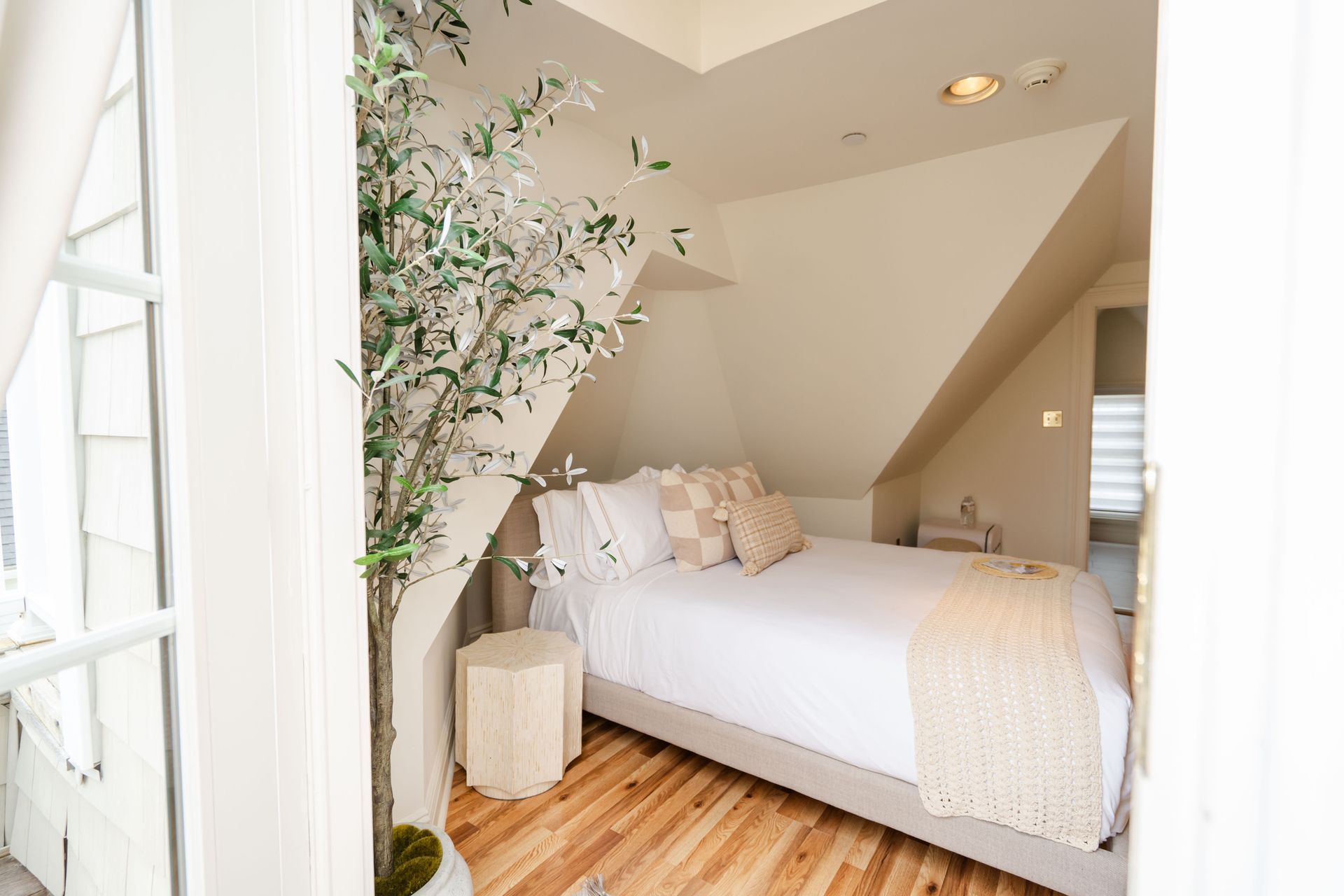 Bedroom with angled ceiling, bed, wooden floor, and a tall, leafy plant.