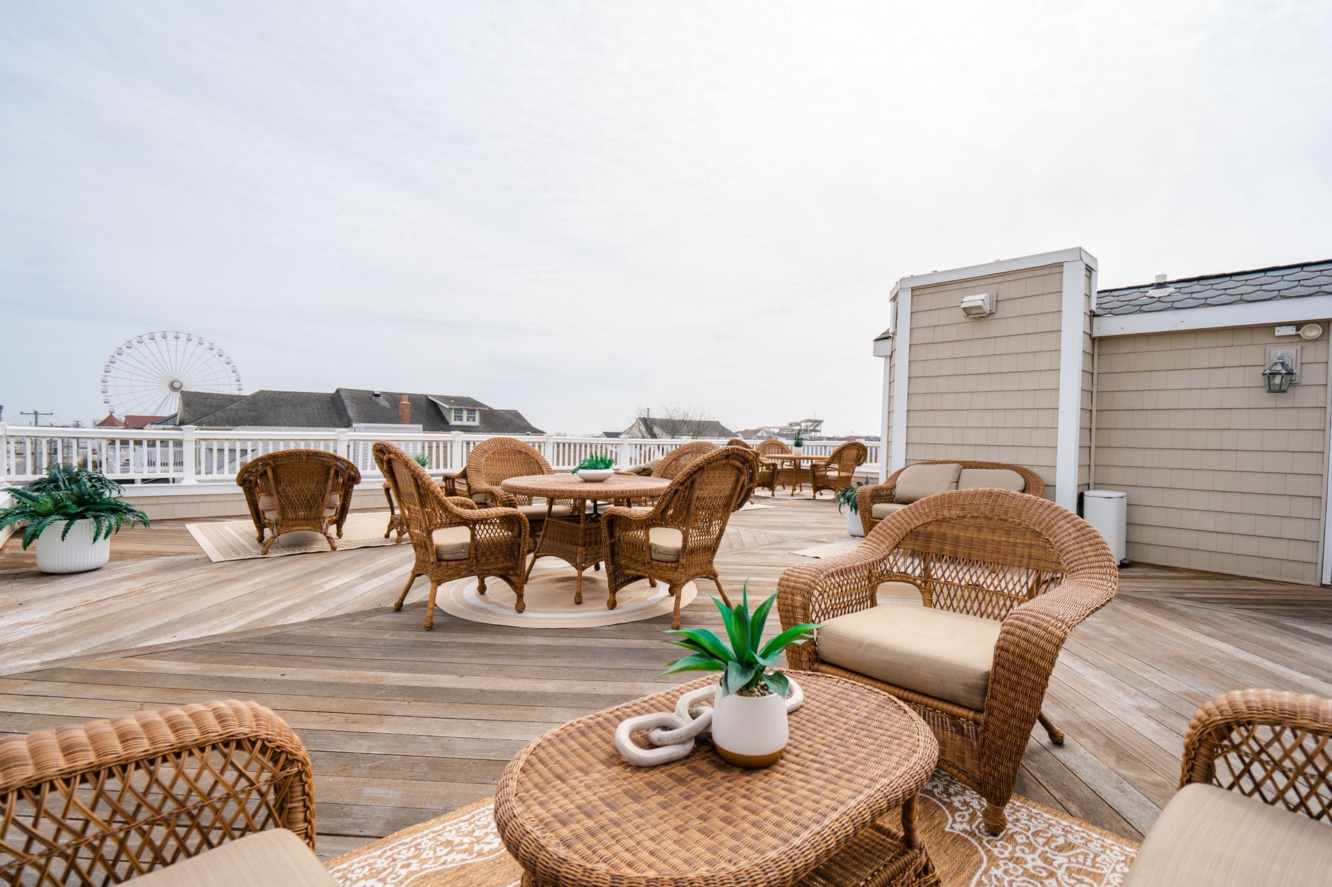 Rooftop deck with wicker furniture, round table, and plants; Ferris wheel in the background.