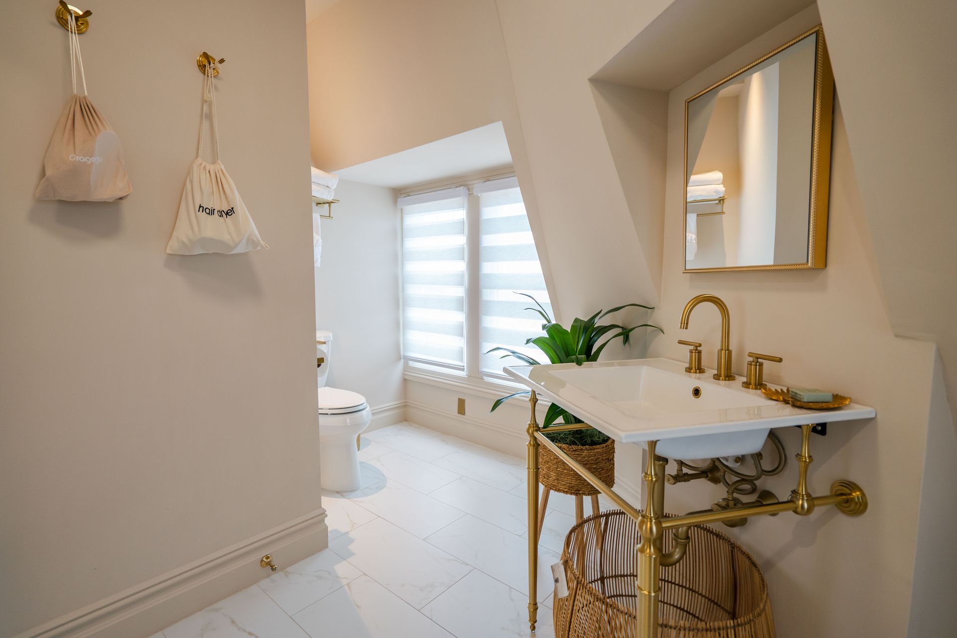 Bathroom with white walls and floor, gold fixtures, and a window with blinds.