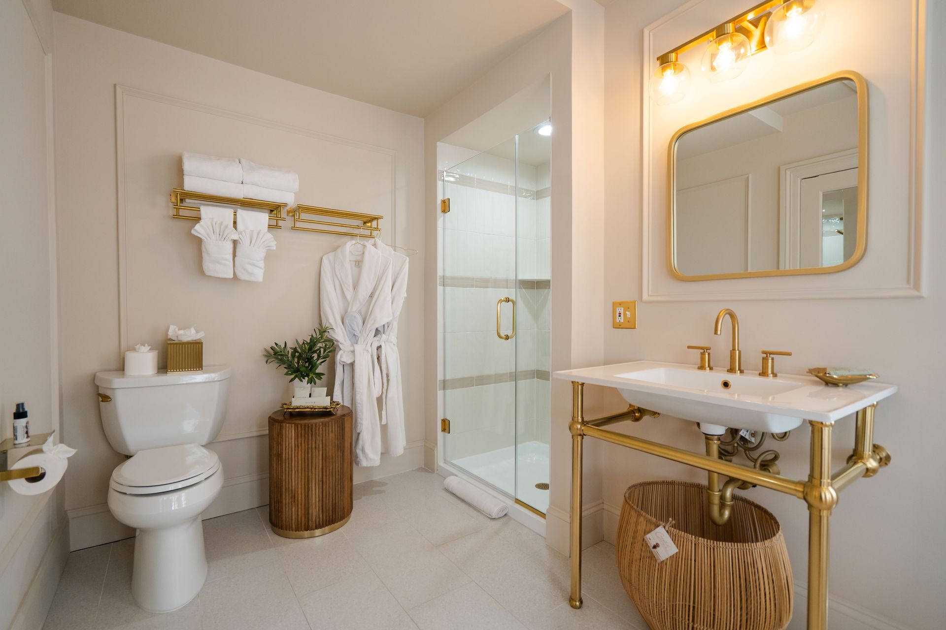Elegant bathroom with gold fixtures, marble sink, glass shower, toilet, and white towels.