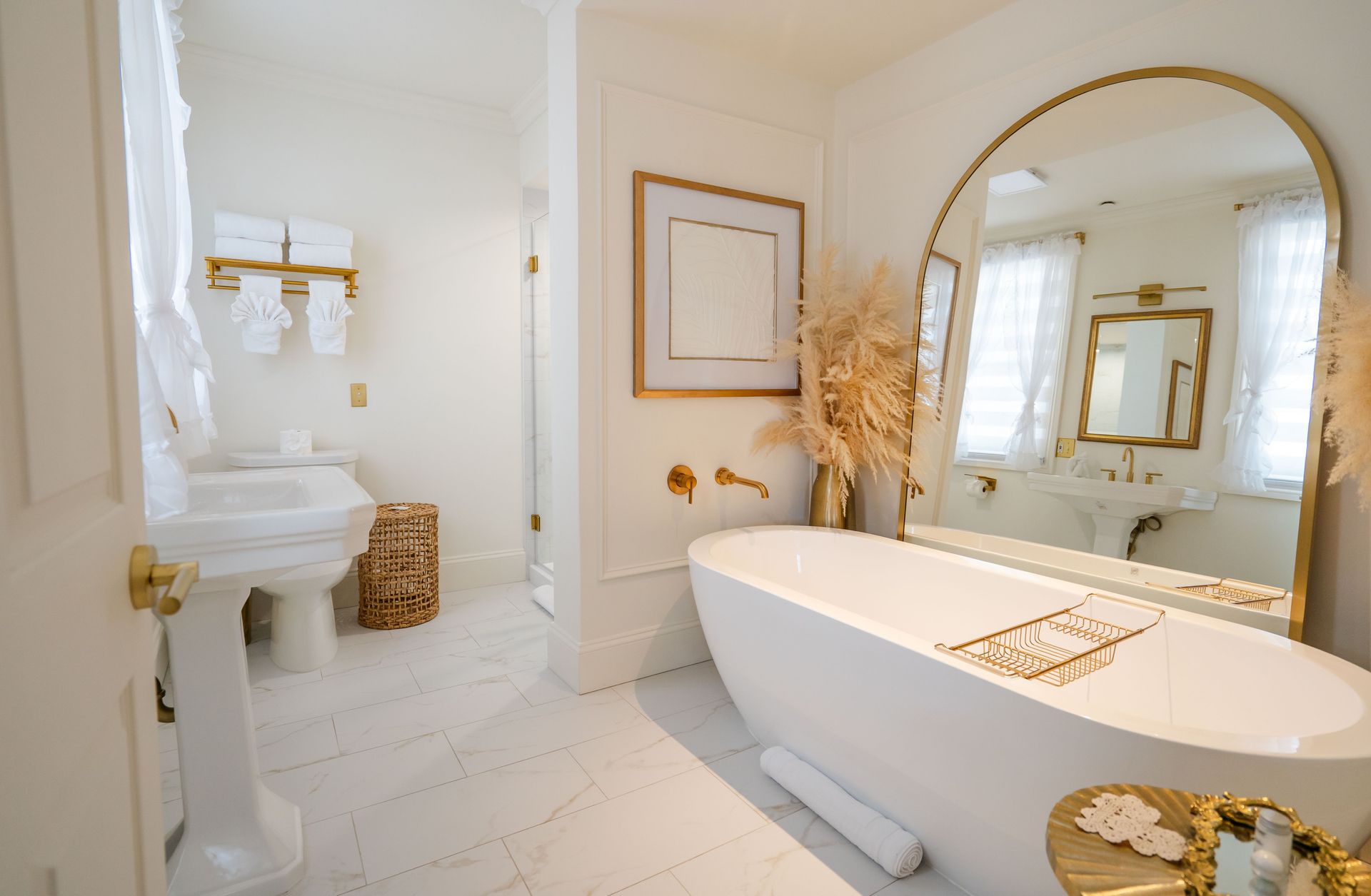 Elegant white bathroom with large arched mirror, freestanding tub, and gold accents.