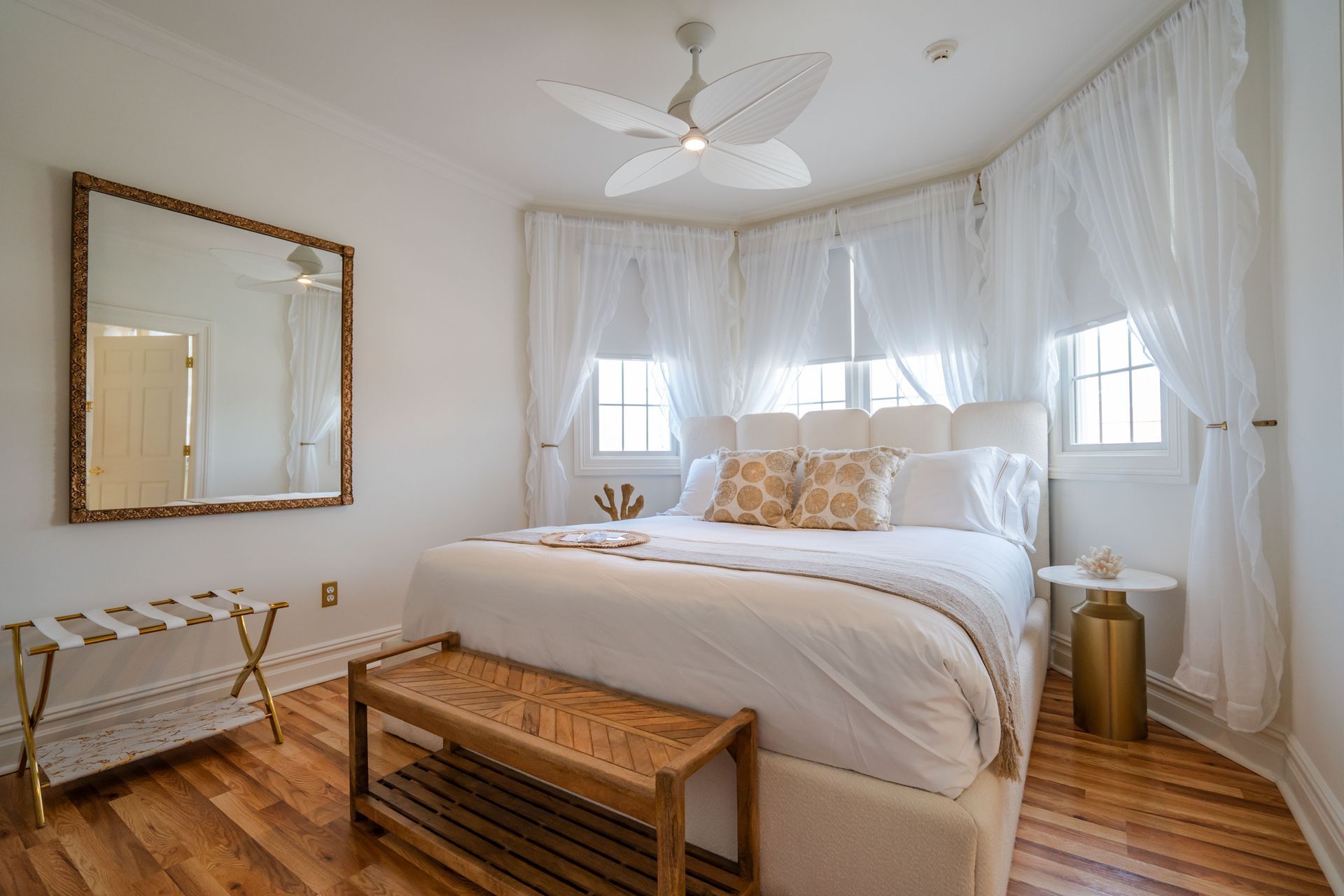 Bedroom with white and gold decor, bed with sheer curtains, a mirror, and a bench.