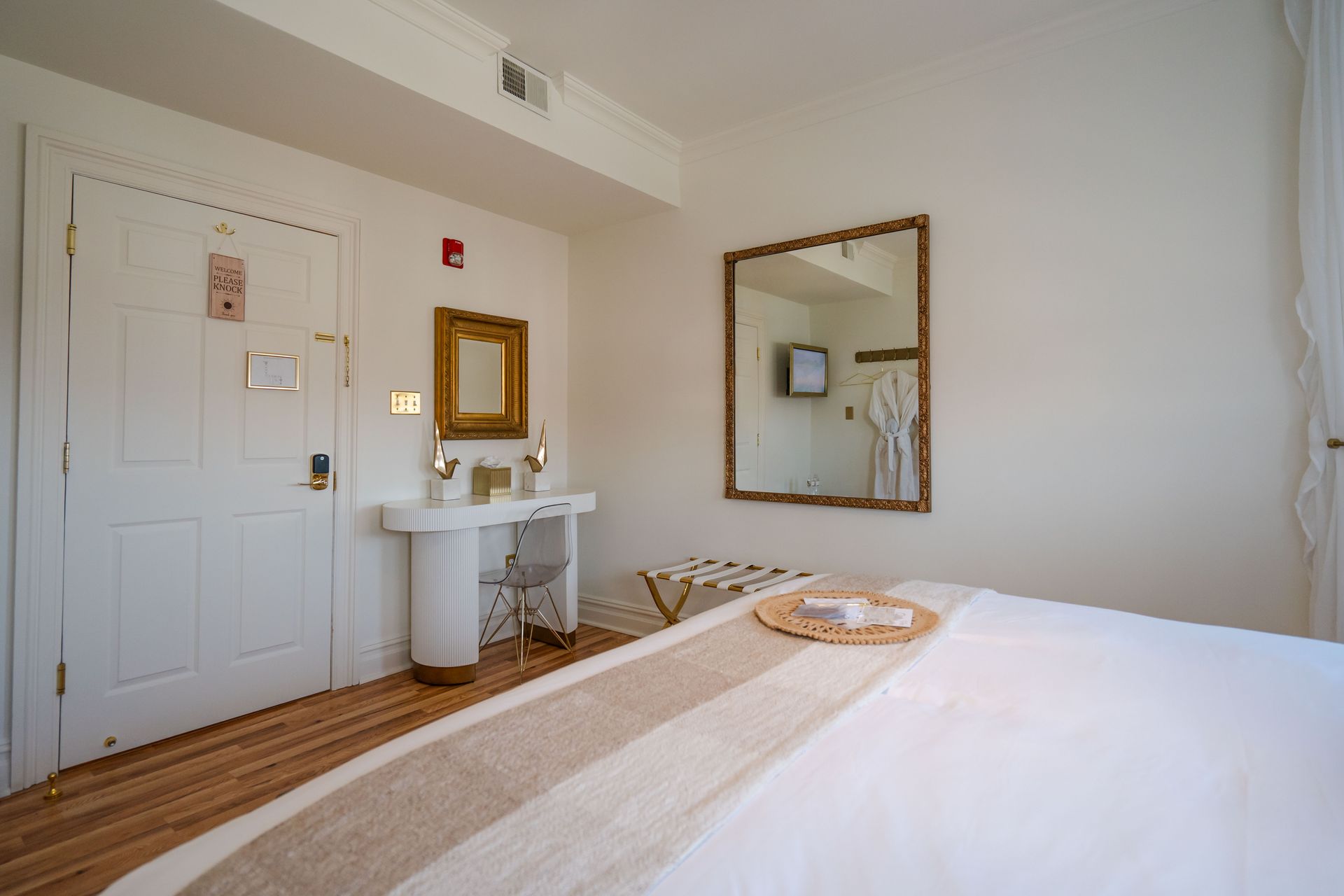 A hotel room with a bed, vanity, mirror, and white door.