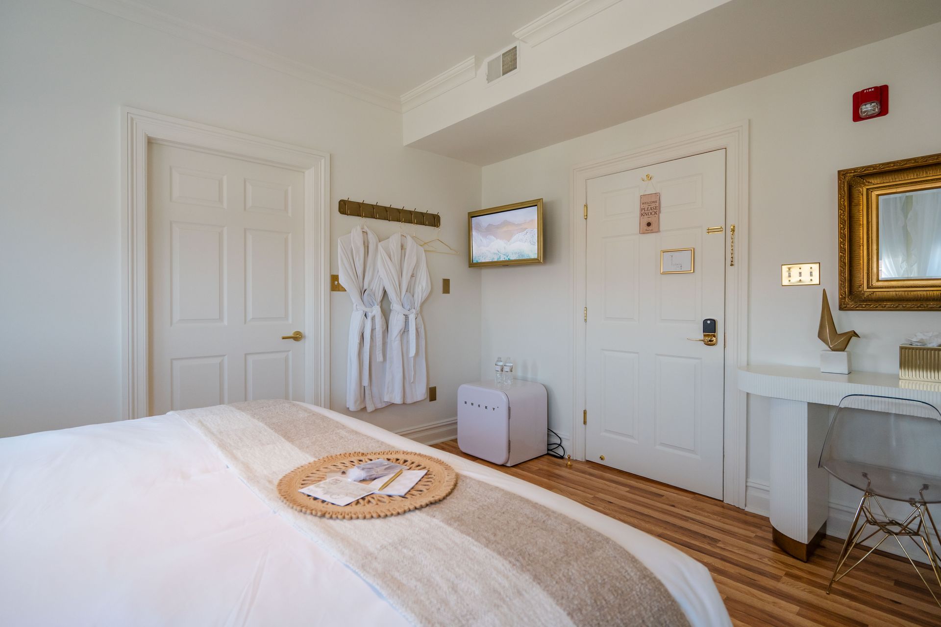 Bedroom with a bed, white doors, and a vanity. Robes hang on the wall.