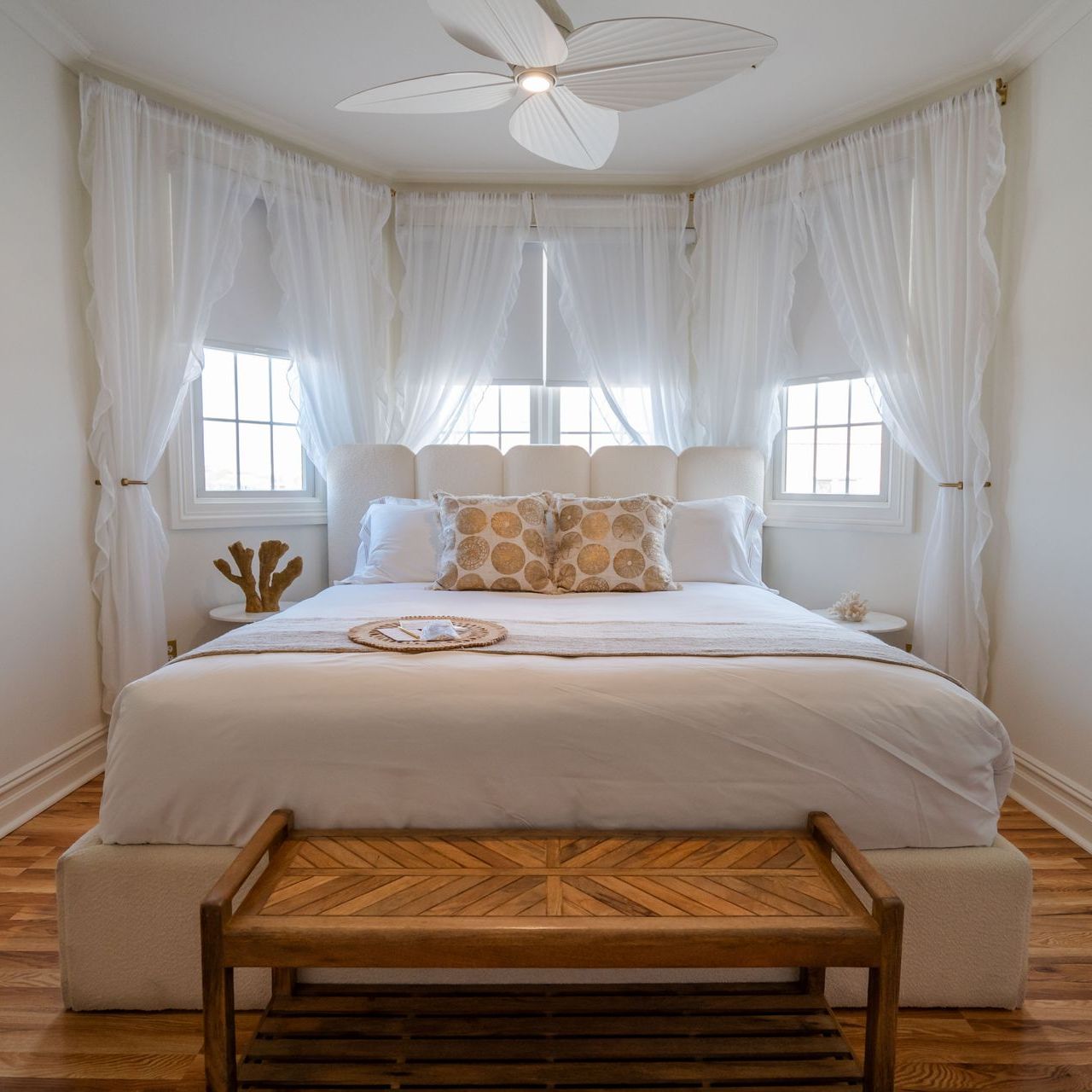 Bedroom with white bed, sheer curtains, and wooden bench.